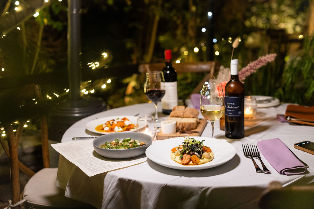 Seasonal plates and wine on a candlelit garden table