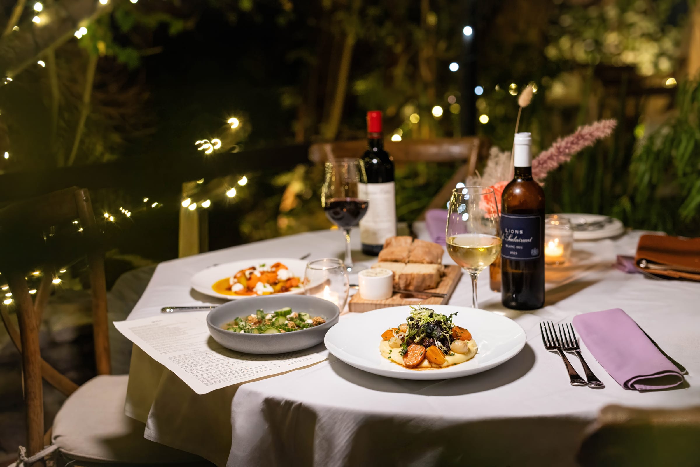 Seasonal plates and wine on a candlelit garden table
